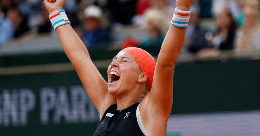 Diana Shnaider celebrating with both arms raised and clenched fists after a tennis victory on court.