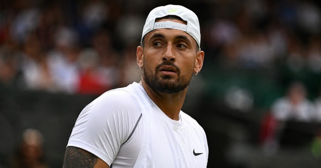 Nick Kyrgios looks on during a tennis match while wearing a white cap and shirt.